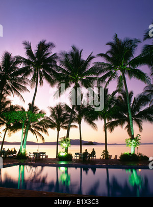 Station tropicale avec des palmiers au bord d'une piscine au coucher du soleil, silhouettes de personnes profitant de la vue Banque D'Images