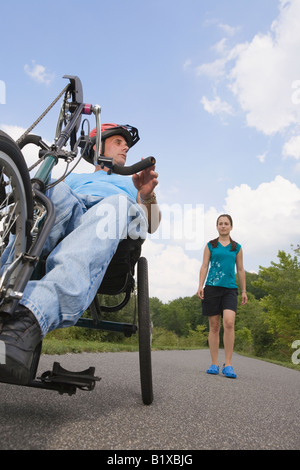 Jeune homme équitation adaptive bike avec une jeune femme debout à l'arrière-plan Banque D'Images