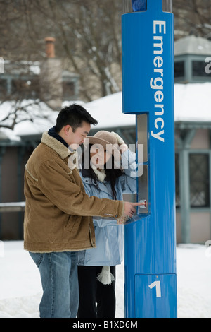 Portrait d'un jeune homme à l'aide d'un téléphone d'urgence à une jeune femme debout à côté de lui Banque D'Images