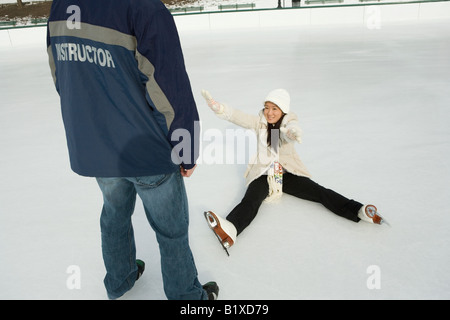 Jeune femme tombée sur une patinoire et donnant la main à un jeune homme Banque D'Images
