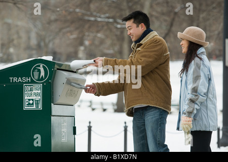 Jeune homme de jeter les ordures dans une poubelle avec une jeune femme se tenant derrière lui Banque D'Images