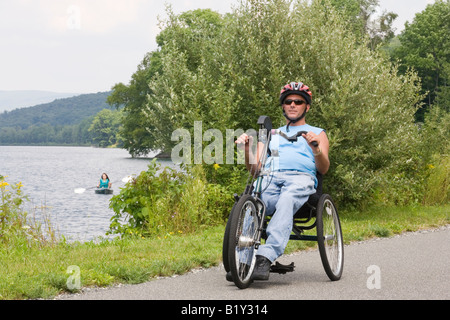 Jeune homme équitation adaptive bike avec une jeune femme kayak dans un lac à l'arrière-plan Banque D'Images