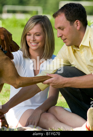 Un jeune couple dans la vingtaine dans le parc avec leur Hungarian Vizsla devint chien sur un dimanche après-midi ensoleillé Banque D'Images