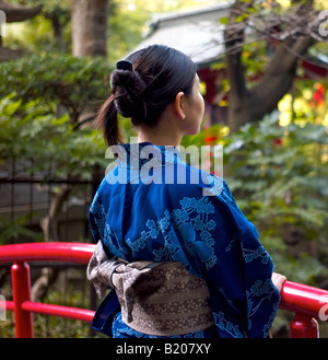 Jeune fille portant un kimono japonais réfléchit sur un pont rouge Banque D'Images