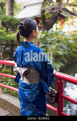 Femme portant un kimono japonais réfléchit sur un pont rouge Banque D'Images