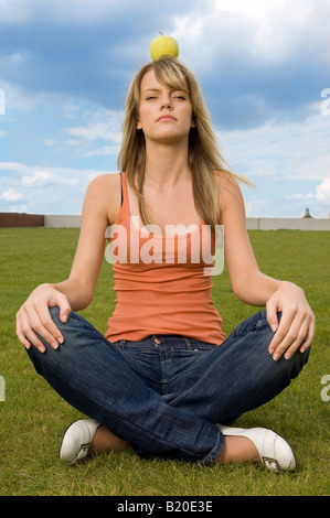 Jeune femme assise avec une pomme sur la tête. Banque D'Images