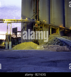 Crépuscule sur matières premières, courroie de transport et de silos à une usine de ciment. Banque D'Images