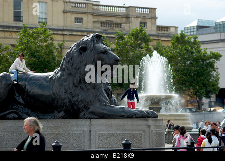 Les touristes de grimper sur l'un des grands lions en bronze qui s'asseoir au pied de Nelsons column à Trafalgar Square à Londres UK Banque D'Images