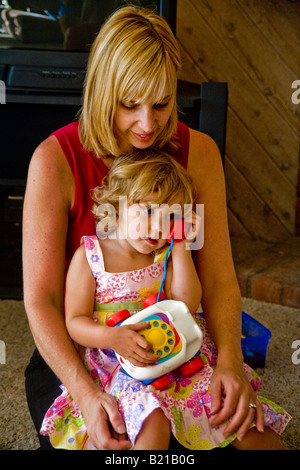 Une fillette de deux ans joue avec toy téléphone alors que sa mère la tient en Californie du Sud Banque D'Images