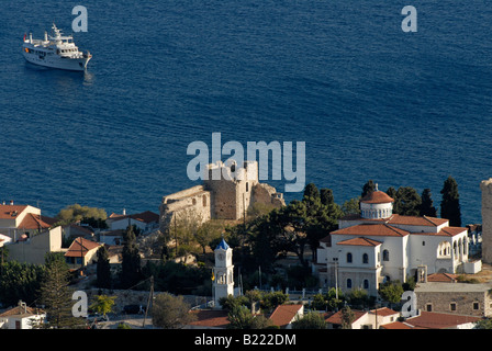 Château grec, église et maisons sur une colline au-dessus de la mer bleue avec un yacht à moteur à l'arrière-plan. Banque D'Images