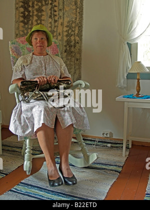 Vieille Femme assise strage bizarre pensive sur le fauteuil à bascule avec un sac à main dans une chambre vétuste Banque D'Images