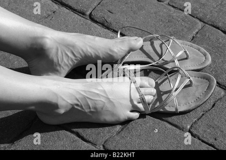 Les pieds de la femme et des sandales et elle prend le soleil sur le trottoir, en noir et blanc. Banque D'Images