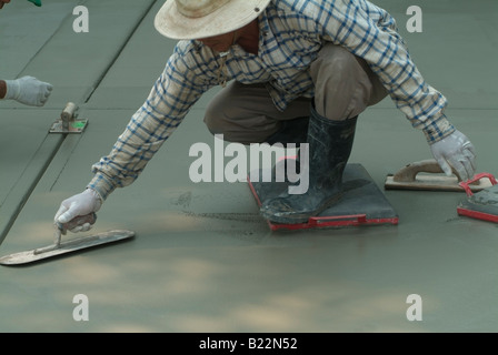 Mise à niveau de l'ouvrier du béton humide avec un Darby tandis qu'un autre ouvrier utilise un outil de chants de gorge de béton fraîchement coulé. Banque D'Images