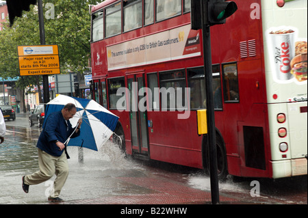 La danse de la pluie : Un homme évite d'être éclaboussé par un bus passant à Lewisham High Street sur un très mauvais jours Banque D'Images