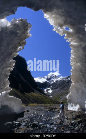 Une silhouette solitaire se dresse à l'entrée d'une grotte de glace formée pendant la fonte des neiges, Milford Road, Fiordland, Nouvelle-Zélande Banque D'Images