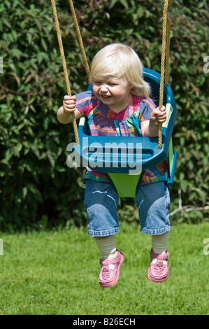 Un mignon jeune fille enfant en riant et s'amusant dans un swing sur une journée ensoleillée. Banque D'Images