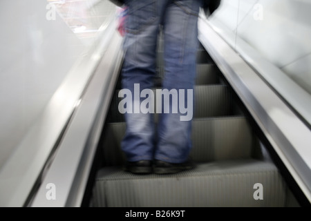 Personne en jeans debout sur déménagement escalator Banque D'Images