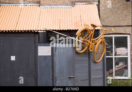 Un vélo peint en jaune clair et fixé sur le côté d'un jeter un atelier de réparation de vélo Banque D'Images