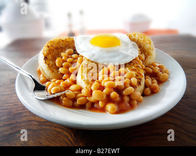 Haricots cuits au four et un œuf frit sur crumpets a servi de repas sur une plaque blanche dans une table Banque D'Images