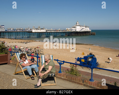 Deux dames s'asseoir dans des chaises longues et discuter dans le soleil d'été sur le front de mer par la jetée d''Eastbourne East Susssex UK Banque D'Images