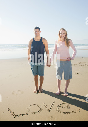 Couple à côté de l'amour écrit dans le sable Banque D'Images