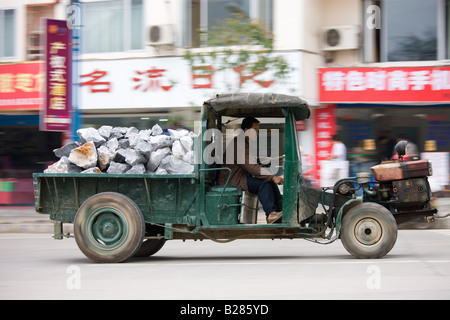 Les lecteurs de l'homme contenant des tas de tracteur livraison des pierres de construction dans la rue Yangshuo Chine Banque D'Images