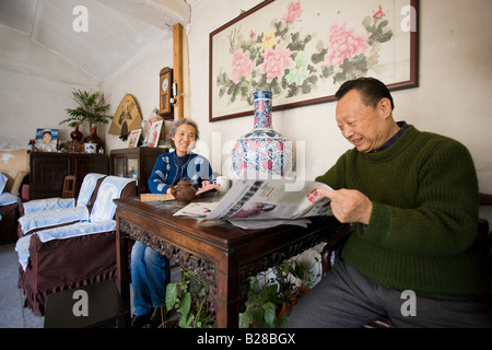 Couple lire un article de journal sur les Jeux Olympiques de Beijing dans leur maison dans les Hutongs de Beijing Chine zone Banque D'Images