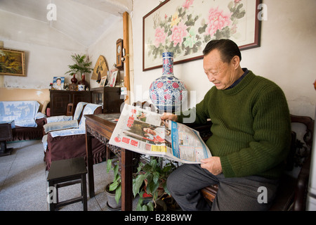 L'homme lit un article de journal sur les Jeux Olympiques de Beijing dans sa maison dans les Hutongs de Beijing Chine zone Banque D'Images