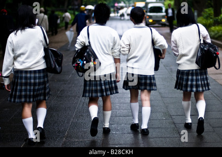 La vue arrière de quatre écolières japonaises en marche une ligne passant par le parc Ueno de Tokyo portant des uniformes scolaires. Banque D'Images