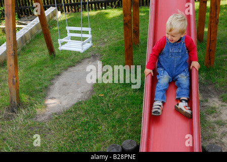 Bébé garçon blond glissant sur la diapositive sur l'aire de jeux Banque D'Images