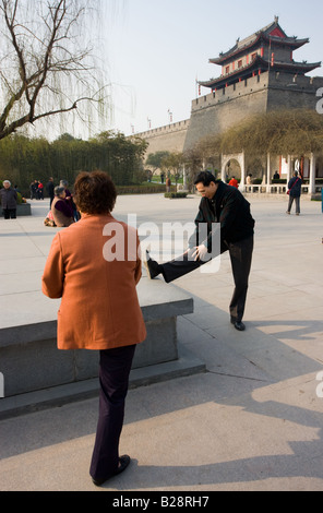 Les gens qui s'étend avant de pratiquer le tai-chi dans le cadre de leurs exercices matinaux dans le parc par le mur de la ville Xian Chine Banque D'Images