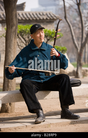 L'homme joue un Erhu, instrument à l'aide d'un arc dans le parc par le mur de la ville Xian Chine Banque D'Images