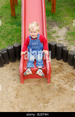 Bébé garçon blond glissant sur la diapositive sur l'aire de jeux Banque D'Images