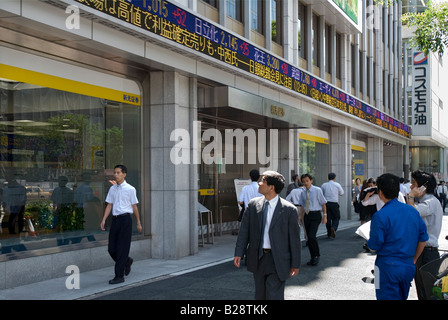 Hommes d'adoption d'une société de valeurs mobilières de Tokyo afficher les derniers chiffres boursiers sur une bande du téléscripteur électronique de plein air Banque D'Images