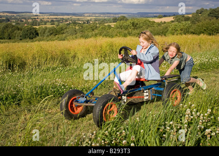 Deux jeunes filles s'amusant sur la pédale chariot d'aller en champ agricole Cotswolds UK Banque D'Images