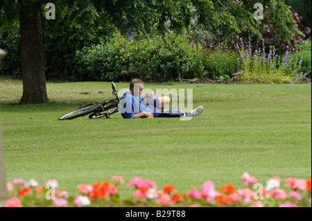 Les gens dans le Parc : Un cycliste fatigué prend un repos et de verre sur l'herbe à Sheffield's Botanical Gardens. Banque D'Images