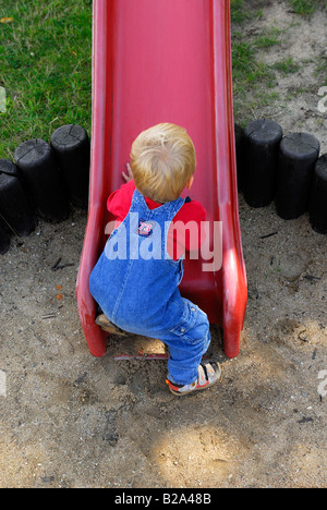 Bébé garçon blond glissant sur la diapositive sur l'aire de jeux Banque D'Images