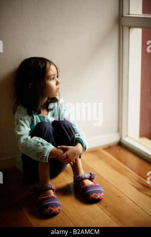 Portrait de petite fille âgée de cinq ans s'assit sur le plancher à côté de fenêtre mixed race caucasienne et ethnique indien Banque D'Images