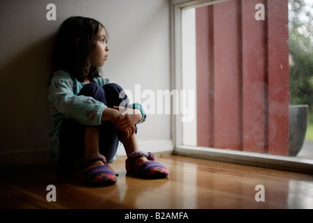 Portrait de petite fille âgée de cinq ans s'assit sur le plancher à côté de fenêtre mixed race caucasienne et ethnique indien Banque D'Images