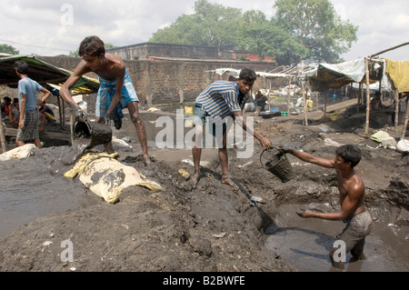 Habitants de taudis vivant au milieu de recyclage de déchets industriels, les jeunes hommes versant industriels lavés dans une rangée de parpaing de hol Banque D'Images