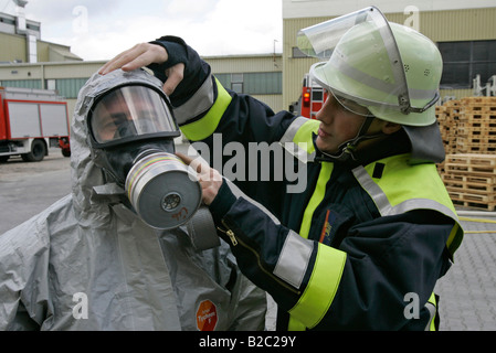 Aider un collègue pompier mis sur un ensemble de protection en cas de catastrophe au cours d'une perceuse, près de Poing, Bavaria, Germany, Europe Banque D'Images