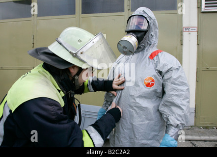 Aider un collègue pompier mis sur un ensemble de protection en cas de catastrophe au cours d'une perceuse, près de Poing, Bavaria, Germany, Europe Banque D'Images