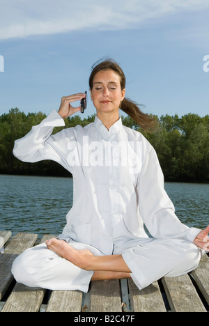 Woman practicing Yoga, demi-lotus pose, Ardha Padmasana, Mudra et phoning Banque D'Images