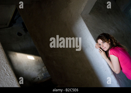 Jolie jeune femme aux cheveux bouclés brun et rose top, appuyé contre un mur Banque D'Images