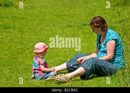 Portrait horizontal de 18 mois, petite fille assise dans l'herbe à la campagne avec sa mère sur journée ensoleillée Banque D'Images