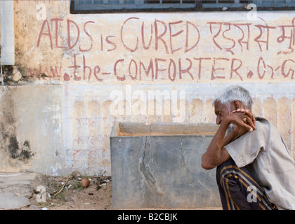 Un homme âgé est assis en face d'un mur à Pushkar Inde sur le mur est écrit le SIDA est guéri Banque D'Images