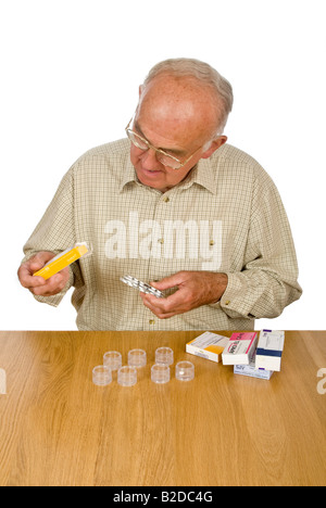 Portrait vertical d'un vieux monsieur l'organisation de son médicament hebdomadaire en conteneurs individuels dans le cadre d'une tour de stockage. Banque D'Images