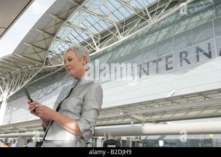 Mature Woman using phone en face de l'aéroport. Banque D'Images