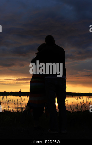 Happy young couple holding les uns les autres et en regardant le coucher de soleil silhoutte of mountain range at sunset à fixer contre le soleil couchant Banque D'Images