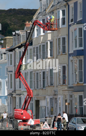 Man on cherry picker plate-forme surélevée, l'inspection de la façade des maisons en terrasse à Aberystwyth Wales UK Banque D'Images